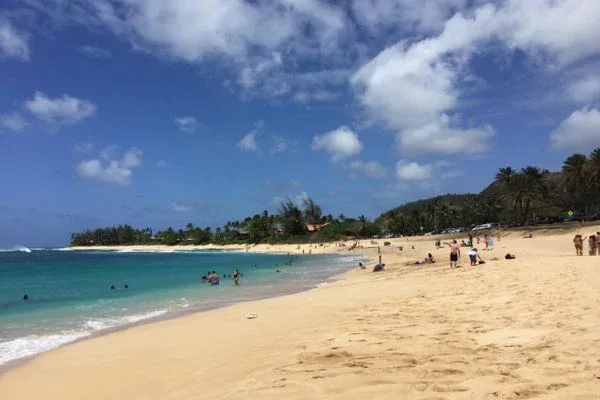 People enjoying a sunny day at Sunset Beach Park, swimming and relaxing on the sandy shore.