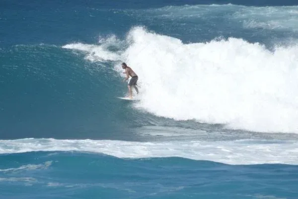 A surfer catching a wave at Sunset Beach Park, showcasing the strong surf and clear blue water