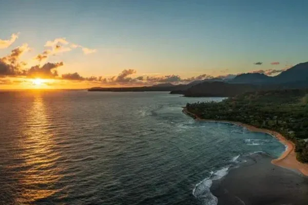 A coastal view at sunset with the sun dipping below the horizon, casting a golden glow over the ocean waves and the distant shoreline.