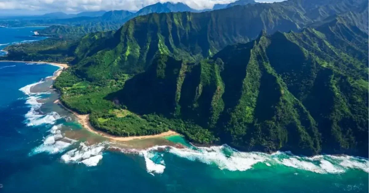 The image you uploaded appears to be of a stunning coastline with lush green mountains and clear blue waters. This landscape is characteristic of the Na Pali Coast on the island of Kauai, Hawaii, particularly near Tunnels Beach, known for its dramatic cliffs and beautiful beaches.