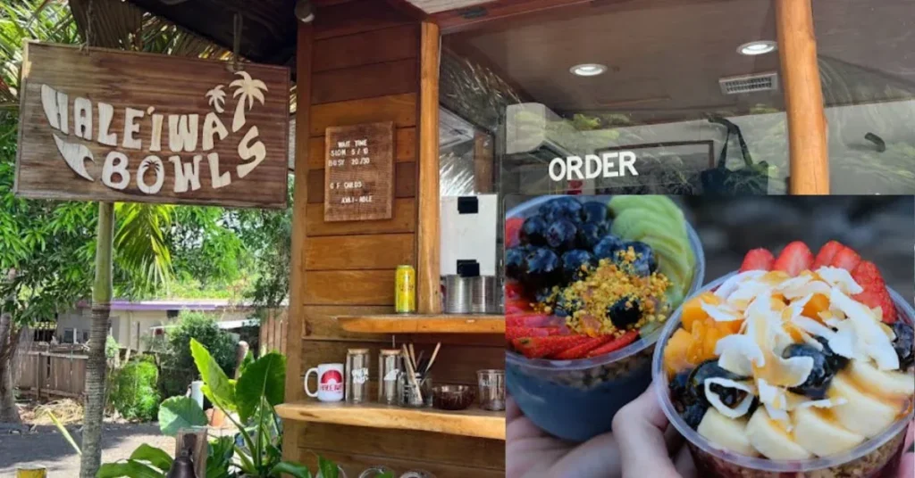 The exterior of Haleʻiwa Bowls, a wooden smoothie and acai bowl shack located at 66-030 Kamehameha Hwy, Haleiwa, HI 96712, United States. The wooden sign with the name "Haleʻiwa Bowls" hangs above the entrance, surrounded by lush greenery. Below the sign, a counter is visible with various items. On the right side of the image, two colorful acai bowls topped with fresh fruits like blueberries, strawberries, bananas, kiwi, and shredded coconut are shown, highlighting the delicious offerings from the shop.